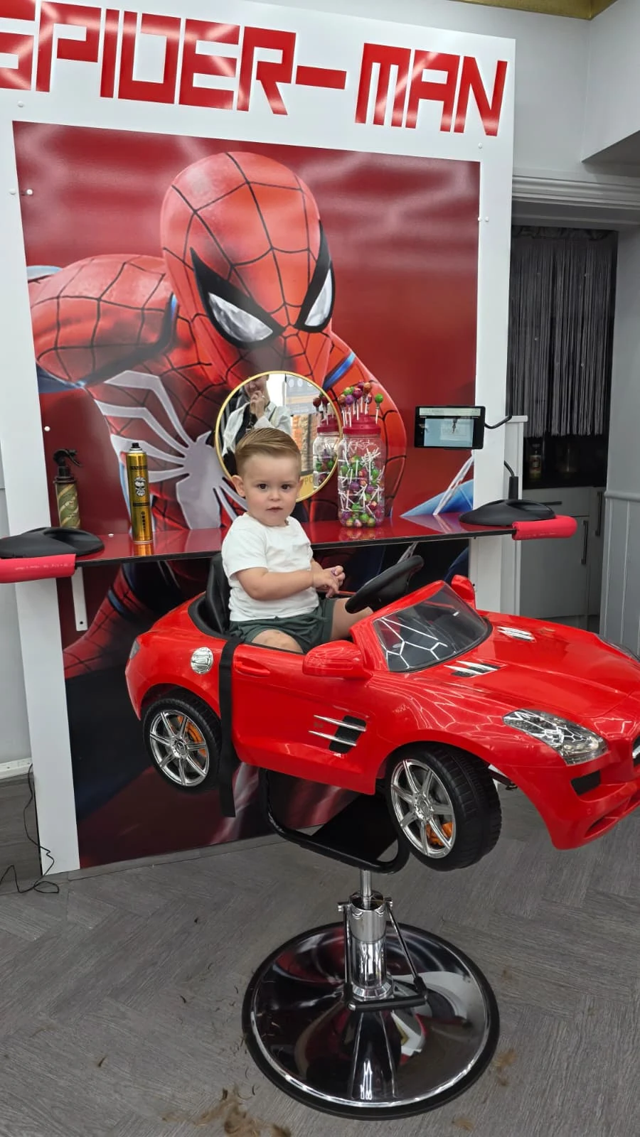 Child sitting in the red Spider-Man barber car